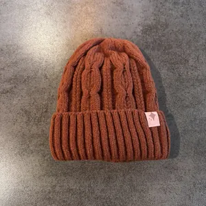 Dettaglio cappello invernale a trecce spesse con risvolto a coste e toppa con stella