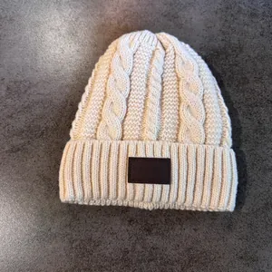 Detail van beige gebreide muts met kabelpatroon en leren patch op de geribde rand