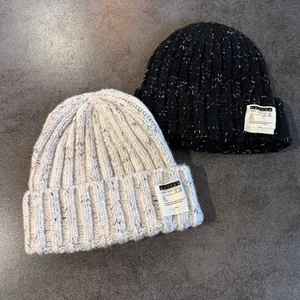 Detail of chunky knit beanies in black and beige with logo patches and speckled texture