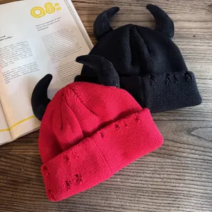 Close-up of distressed knit beanie with devil horns and pin details on wooden surface