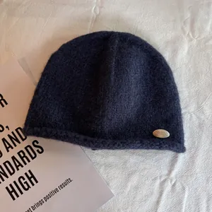 Detail shot of navy blue wool knit beanie featuring a silver metal logo and rolled edge