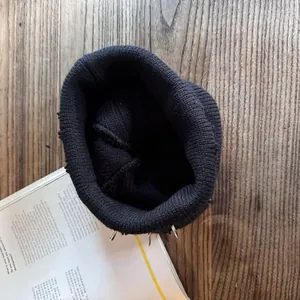 Detail of black distressed beanie featuring silver metal rings in a street punk style