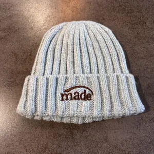 Détail du bonnet en maille côtelée bleu clair avec broderie marron sur table en bois