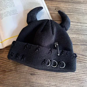 Detail of black knit beanie featuring devil horns, distressed holes, and silver metal pins