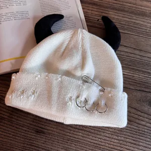 Detail of white knit beanie with black demon horns and punk metal safety pin safety