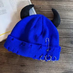 Detail of blue distressed knit beanie with black devil horns and silver metal safety pins