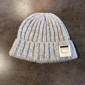 Close-up of thick grey knit beanie featuring a white letter patch and ribbed texture