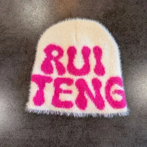 Detail of soft cream faux mink beanie featuring a vibrant pink embroidered letter logo