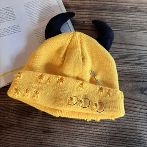 Detail of yellow distressed beanie with black horns, safety pins and metal rings