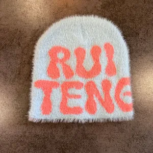 Close-up of light blue faux fur beanie featuring orange RUI TENG jacquard lettering