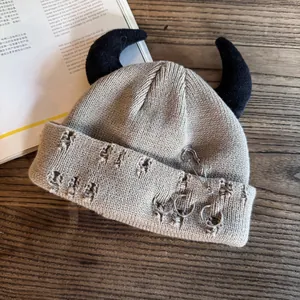 Detail of khaki distressed knit beanie featuring punk horns and silver metal pin accents