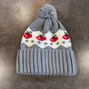 Dettaglio del cappello in maglia grigia con motivi a fragola e pompon morbido