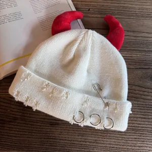 Detail of white distressed beanie with red devil horns, metal pin and silver ring accents
