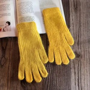 Detail view of ginger yellow knitted plush gloves on a wooden table with a magazine