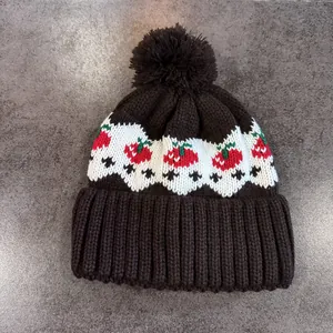 Dettaglio del berretto in maglia con motivo jacquard fragola e pompon in pelliccia nera