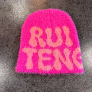 Close-up of fluffy faux mink fuchsia beanie with knit RUI TENG lettering on stone background