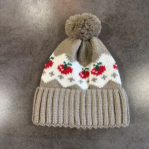 Dettaglio ravvicinato del cappello in maglia con motivi a onde bianche e decori a ciliegia