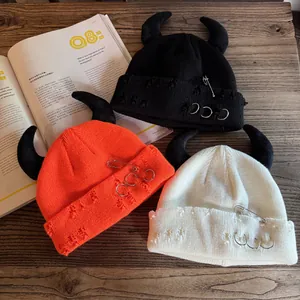 Distressed knit beanies with devil horns, safety pins and rings in black, orange and cream