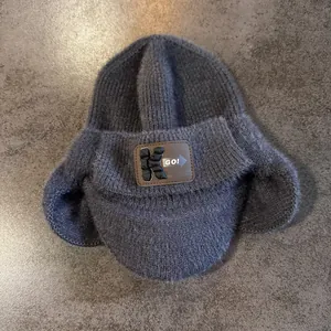 Détail d'un bonnet en tricot gris foncé avec texture duveteuse et écusson en cuir style K