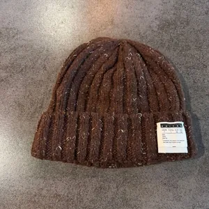 Detail of chunky knit beanie with white logo patch and textured salt and pepper yarn