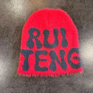 Close-up of red faux mink fur beanie with navy blue RUI TENG knitted letter pattern