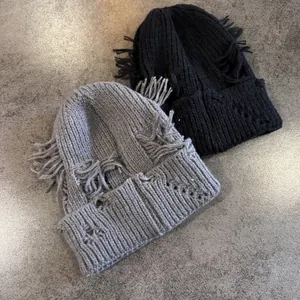 Primer plano de gorros de punto desgastados con agujeros y flecos en gris y negro