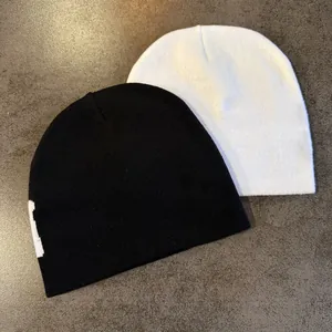 Flat lay of black and white jacquard knit beanies with minimalist letter patterns