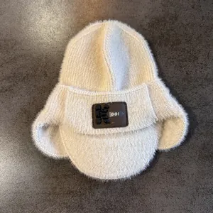 Détail du bonnet en maille blanche avec texture duveteuse et écusson en cuir brun