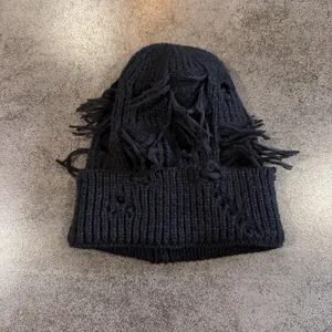 Vista detallada del gorro de punto negro con diseño desgastado y bordes deshilachados urbanos