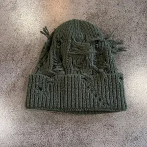Detalle del gorro de punto verde oliva oscuro con agujeros desgastados y estilo punk calle