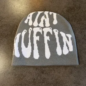 Flat lay of gray knit beanie with white AINT MUFFIN jacquard lettering on wood table