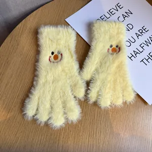 Détail de gants en peluche tricotés jaunes avec un motif de smiley brodé