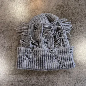 Primer plano de gorro de punto gris desgastado con detalles de rotos y flecos largos