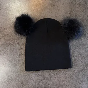 Detalle de gorro de punto negro con dos pompones grandes de piel sintética sobre piedra