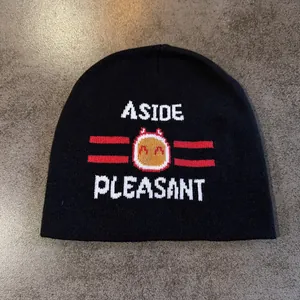 Close-up of black knit beanie featuring white ASIDE lettering and red cartoon fireball jacquard