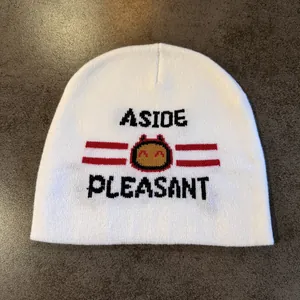 Close-up of white knit beanie with black jacquard lettering and cartoon robot character
