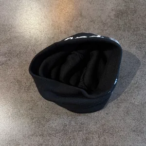 Détail de la texture en maille noire et de la broderie de lettres blanches du bonnet