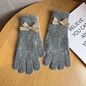 Detail of grey plush knit gloves featuring a cute khaki bow and rib-knit cuffs on wood surface
