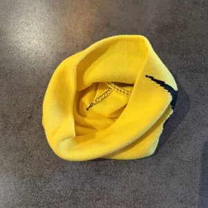 Nahaufnahme einer gelben Strickmütze mit schwarzer Naht und grafischen Details
