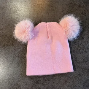 Detalle del gorro de punto rosa con dos grandes pompones de piel sintética en la parte superior