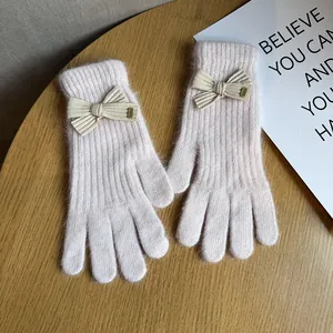 Close-up of pink knit gloves with plush bow and small Baby label on a wooden surface