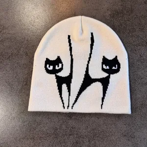 Detailansicht der cremefarbenen Strickmütze mit schwarzen Katzen-Jacquardmustern