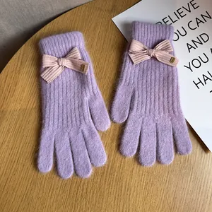 Detail of purple knitted gloves with pink striped bow and small golden Baby metal tag