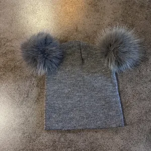 Detalle del tejido de un gorro gris con dos grandes pompones de piel sintética suave