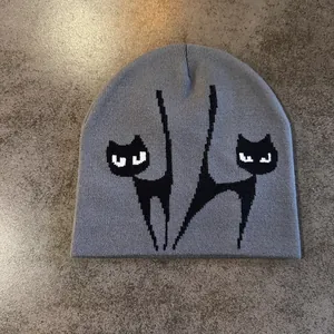 Detail der grauen Strickmütze mit schwarzem Katzen-Jacquardmuster und Pixel-Ohren-Details
