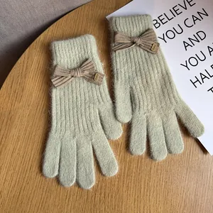 Close-up of green knit gloves with a brown bow and baby engraved metal buckle