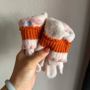 Détail de gants tricotés patte de chat crème avec coussinets roses et poignets orange