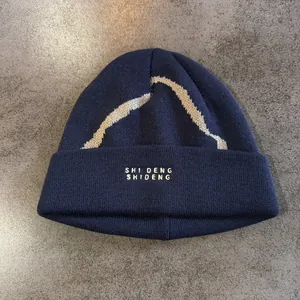Detailopname van een donkerblauwe gebreide muts met witte golfpatronen en borduursels