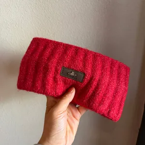 Detail showing red knitted headband with branded leather tag and ribbed wool texture