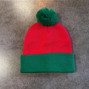 Close-up of red and green knit beanie with a green pompom on a stone texture